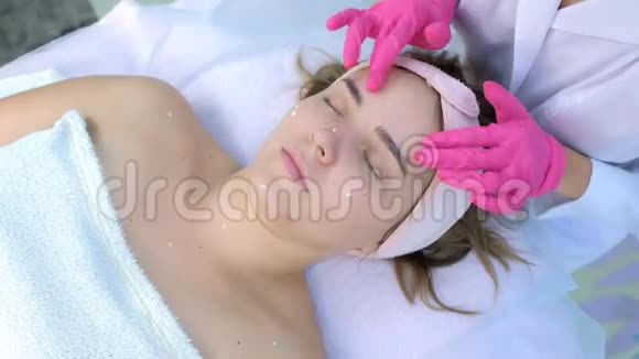 手套美容师正在给客户女性面部按摩皮肤涂霜视频的预览图