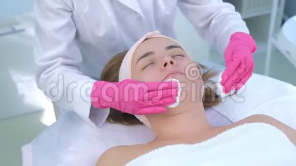美容医生她的手去皮擦拭女人的脸棉花垫在美容诊所视频的预览图