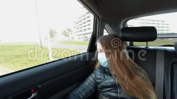 戴口罩的无聊病女孩坐在汽车后座看着车窗视频的预览图