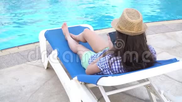 美丽的女人躺在游泳池附近的日光浴床上用手机浏览互联网输入信息享受暑假视频的预览图