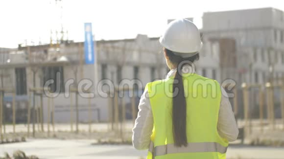 一个年轻的女建筑工人站在施工现场并控制工作流程的背面视图视频的预览图