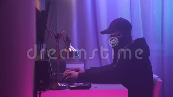 男性黑客坐在办公桌旁闯入系统黑色连帽衫黑色头巾遮住脸视频的预览图