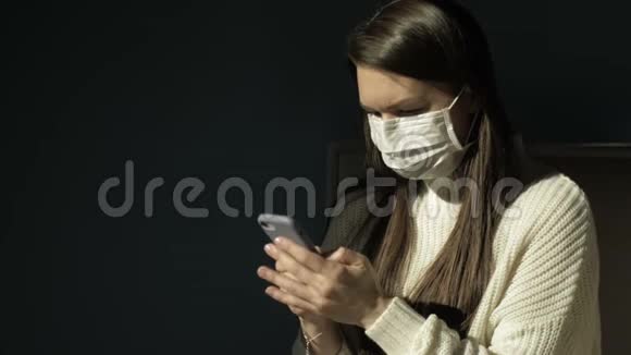 脸上戴着医用口罩的女孩看着手机的屏幕黑暗的背景视频的预览图