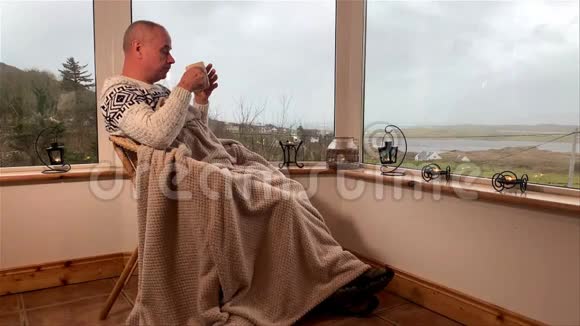 一个人坐在阳台上舒适的柳条椅子上拿着温暖的毯子喝着热茶望着窗外这是一个概念视频的预览图