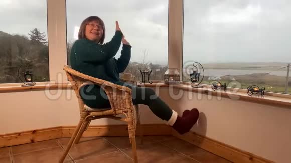 女人坐在一张舒适的柳条椅上坐在山上一个灯光封闭的阳台上享受放松和乐趣伸展她的身体视频的预览图