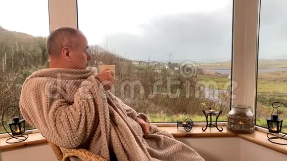 一个人坐在阳台上舒适的柳条椅子上拿着温暖的毯子喝着热茶望着窗外这是一个概念视频的预览图