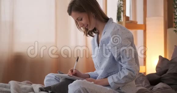 女人坐在床上在家里用记事本写作视频的预览图