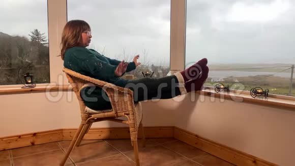 女人坐在一张舒适的柳条椅子上坐在山上一个灯光封闭的阳台上跳舞玩得很开心伸出她的腿在里面视频的预览图