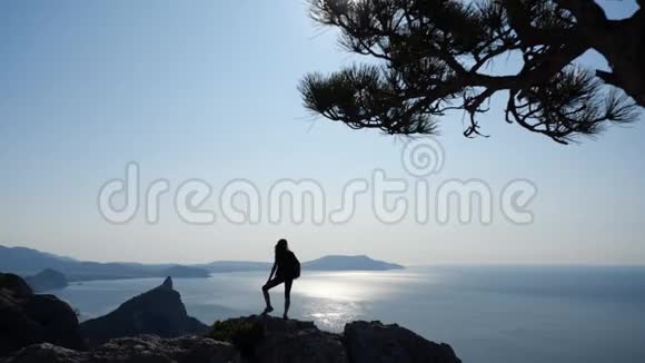 女游客带着背包爬到高高的悬崖顶用太阳和太阳看着美丽的景色视频的预览图