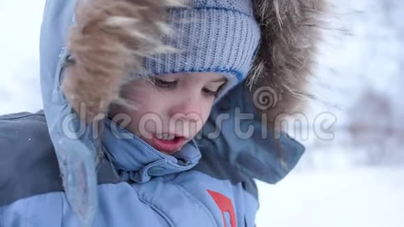一个小孩子在冬季公园散步在白色蓬松的雪上玩耍和微笑的婴儿面的特写积极休息视频的预览图
