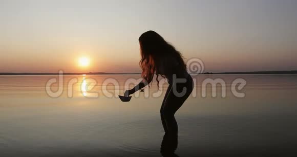 一个留着长长卷发的女孩在水上放下纸船的剪影视频的预览图