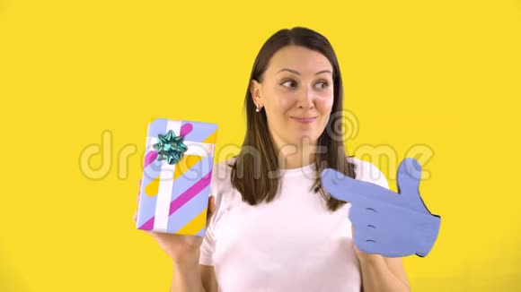 一个穿着白色t恤的年轻女人拿着一个漂亮的盒子和礼物对她露出一个可怕的手指背面黄色视频的预览图