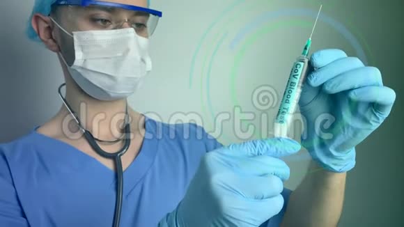 穿着蓝色制服戴着保护面具的听诊器戴着眼镜的男性医生看着一支带血的医用注射器视频的预览图