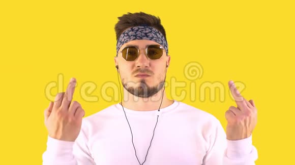 时尚的年轻人戴着时髦的眼镜和手帕用耳机听音乐用中间的手势显示不雅的标志视频的预览图