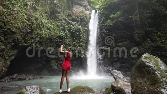 一位年轻的游客站在瀑布前用智能手机捕捉照片视频的预览图