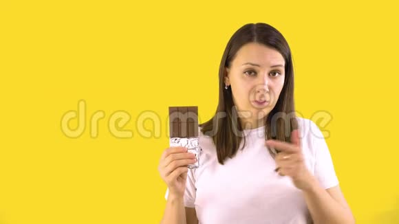 年轻女人拿着巧克力棒说明它是有害的黄色背景人真诚的情感生活方式视频的预览图
