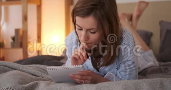 一个体贴的女人躺在床上写着记事本视频的预览图