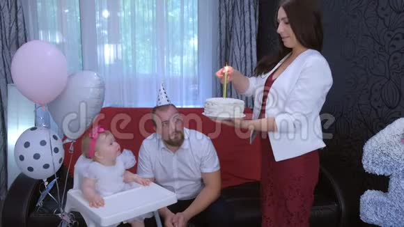 妈妈在生日蛋糕上为一岁的女儿在家里的小女孩点蜡烛视频的预览图