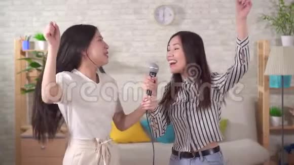 两个年轻的亚洲女人在家里唱卡拉OK视频的预览图