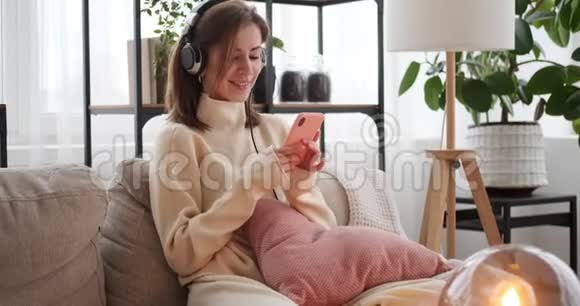 女性在家使用耳机和手机听音乐视频的预览图