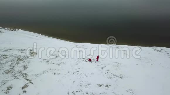 圣诞老人拉着一个雪橇带着一袋礼物沿着雪的海岸顶部视图视频的预览图