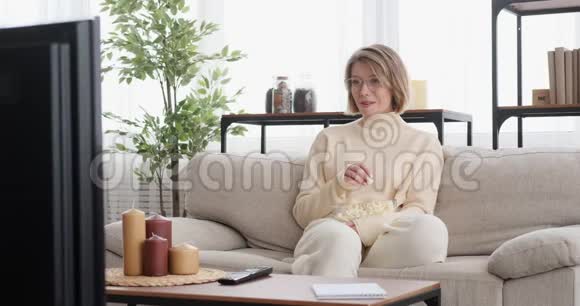 快乐的女人在家看电视吃爆米花视频的预览图