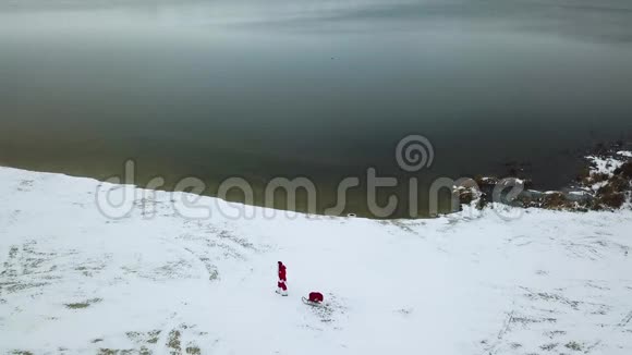 圣诞老人拉着一个雪橇带着一袋礼物沿着雪的海岸顶部视图视频的预览图