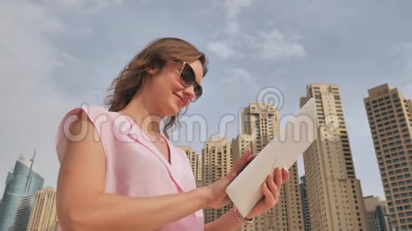 一个欧洲貌美的女孩在迪拜摩天大楼的背景上用平板电脑工作视频的预览图