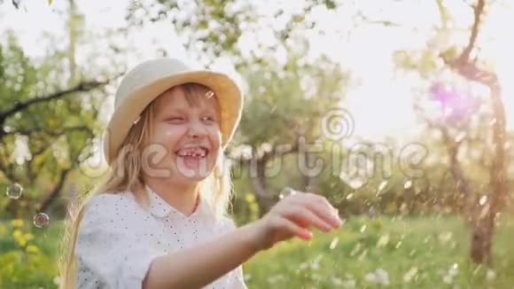 一个戴帽子的快乐女孩漫不经心地玩肥皂泡春天快乐天气好视频的预览图