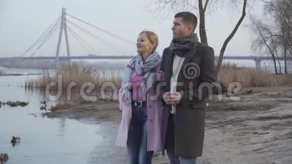 快乐的白人夫妇年龄差异沿着河岸在城市公园散步正面成年男子肖像视频的预览图