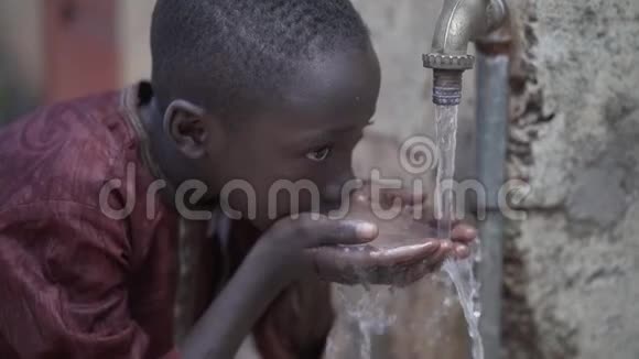 非洲黑人小男孩在水龙头边喝酒的慢镜头视频的预览图