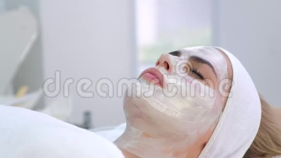女性躺在水疗沙龙的肖像脸上戴着白色面具底部景色视频的预览图