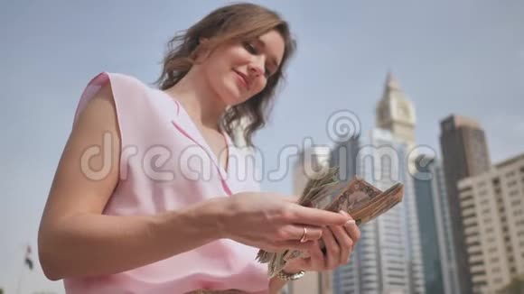 这个女孩在迪拜市中心的背景下手里拿着阿拉伯联合酋长国的钱视频的预览图