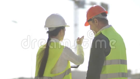 一名男子和一名年轻女子在一个建筑工地戴着头盔和信号背心女人向她汇报一些事情视频的预览图