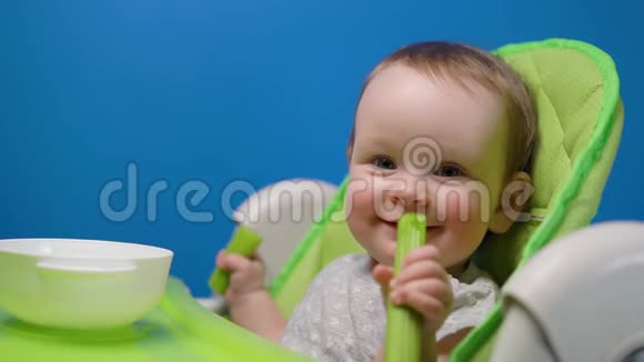可爱的女婴吃着绿色的新鲜芹菜棒看着镜头视频的预览图