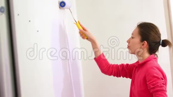 年轻的亚洲幸福女人在新房子里用油漆辊画内墙视频的预览图