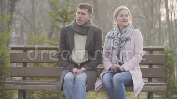 城市公园里坐在长凳上的害羞成年白种人夫妇的肖像年轻男子和年长妇女视频的预览图
