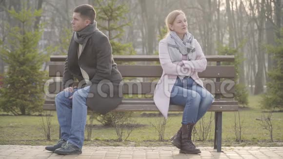 愤怒的白种人男人和女人背靠背坐在户外长凳的对面年纪不大的夫妻视频的预览图