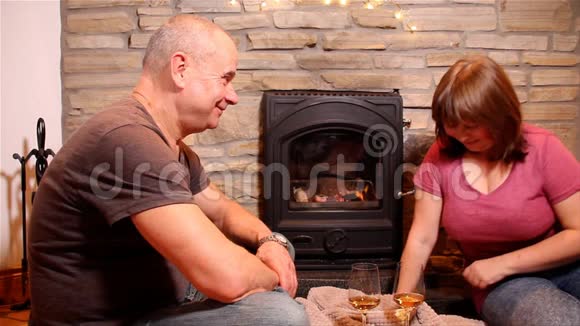女人和男人在燃烧的壁炉前拿着两杯酒这是一个浪漫的夜晚的概念视频的预览图