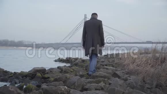 秋日白人成年男子在岩石河岸漫步孤独悲伤的家伙独自在户外视频的预览图