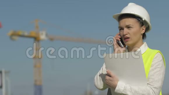 戴着头盔的建筑工女手拿着文件夹在电话里交谈成功的商界女性视频的预览图