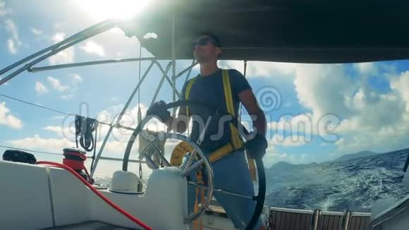 一个戴墨镜的人正在处理帆船的车轮由一个年轻人控制的海洋帆船视频的预览图