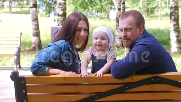 一家人妈妈宝贝女儿和爸爸坐在公园的长凳上微笑着看着摄像机视频的预览图