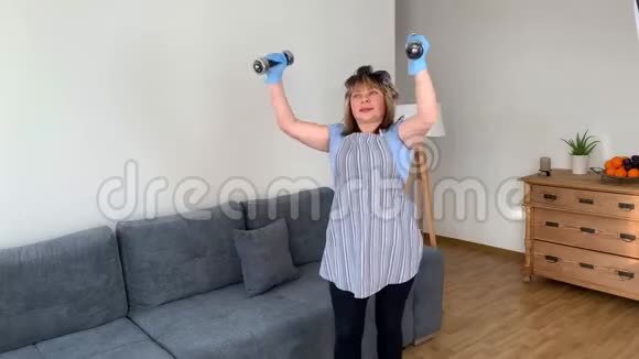 肥胖的中年妇女一个穿着围裙的家庭主妇在家里用哑铃做体育锻炼运动的概念体重视频的预览图