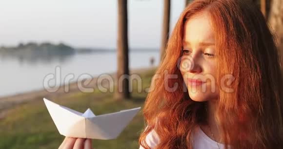 一个红头发的女孩手里拿着一艘白纸船的肖像视频的预览图