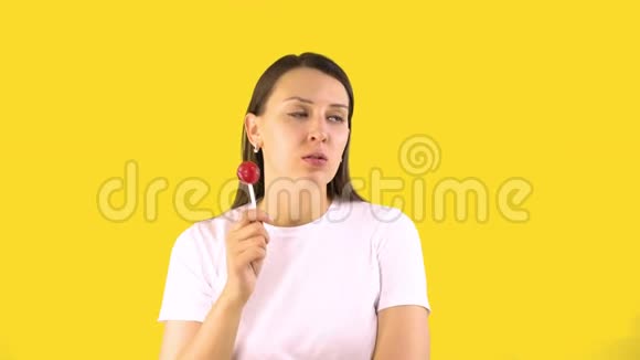 年轻的女人急切地吸着棒棒糖黄色背景人们真诚的情感甜食的概念视频的预览图