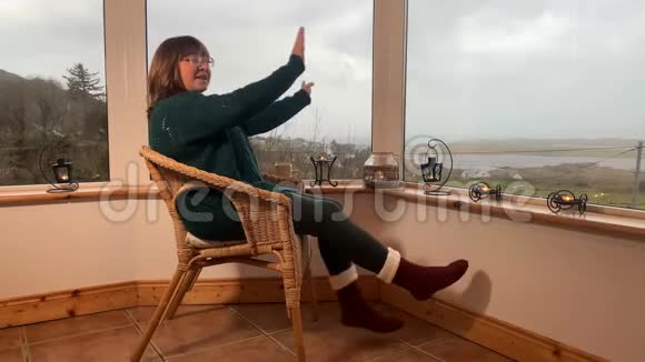 女人坐在一张舒适的柳条椅子上坐在山上一个灯光封闭的阳台上跳舞玩得很开心伸出她的腿在里面视频的预览图