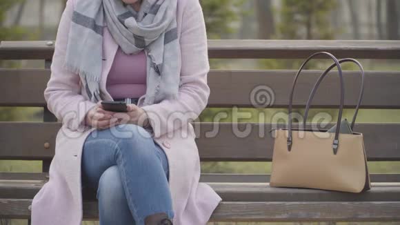 无法辨认的白种人女人坐在户外的长凳上因为男性手在偷她的钱包穿着粉色衣服的漂亮女士视频的预览图