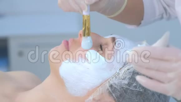 美容师使用刷子侧视将面部保湿面膜涂抹在女性面部视频的预览图