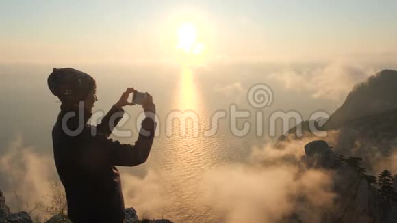 一名身穿头巾的运动旅游妇女站在一座高山的边缘拍摄一张照片视频的预览图